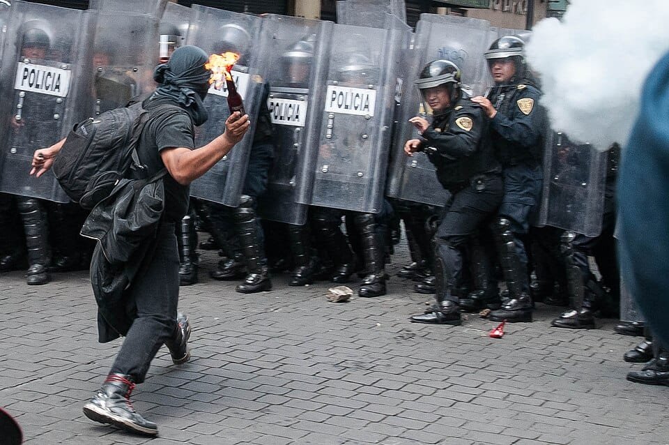 Protester hurling a Molotov cocktail toward riot police in full shields.