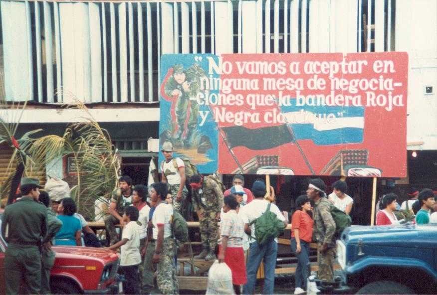Crowd gathered near armed personnel and political banner in León, Nicaragua, during the Sandinista conflict in 1988.