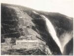 Historic photograph of the Vemork Hydroelectric Plant in Norway, built into a steep mountainside with a large waterfall cascading beside it, known as the primary site of heavy water production during World War II.