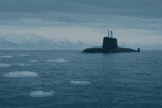 A Soviet-era submarine surfaces in icy Arctic waters with snow-covered mountains in the background and floating ice chunks in the foreground.
