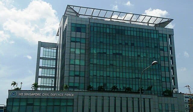 Headquarters building of the Singapore Civil Defence Force, a modern glass-and-steel structure under a partly cloudy sky in Singapore.