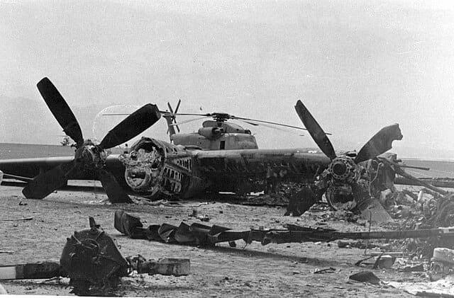 Black-and-white photograph showing the burned wreckage of a U.S. RH-53D helicopter and C-130 transport aircraft at Desert One, Iran, following the failed Operation Eagle Claw hostage rescue mission on April 25, 1980. A key moment in the evolution in elite warfare. 