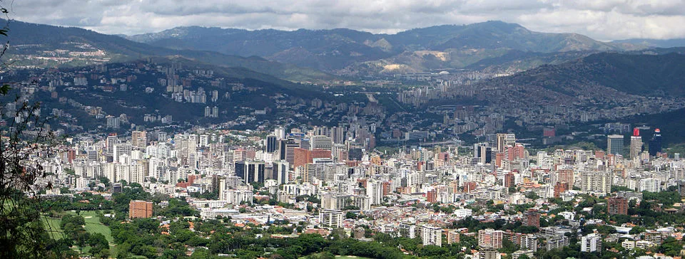Panoramic view of Caracas showing dense high-rise development in the valley surrounded by steep, forested mountains, illustrating the city’s complex megacity terrain and compartmentalized urban structure.