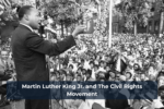 A civil rights leader speaks passionately at an outdoor rally, addressing a large crowd gathered in front of him. The audience, including men, women, and police officers, listens intently as he delivers his speech from a microphone on stage.